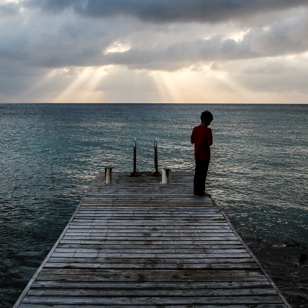 Photo of a boy standing on a pier looking at the sea